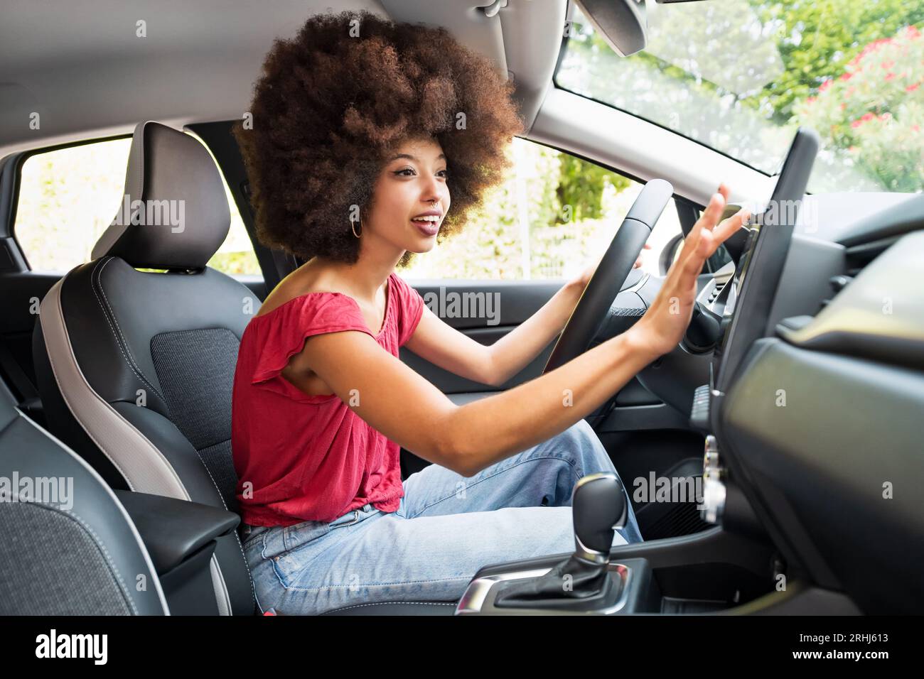 Vista laterale di una giovane donna afro-americana sorridente con i capelli afro che guarda lontano mentre si siede sul sedile del conducente e si imposta la direzione in satellite Foto Stock