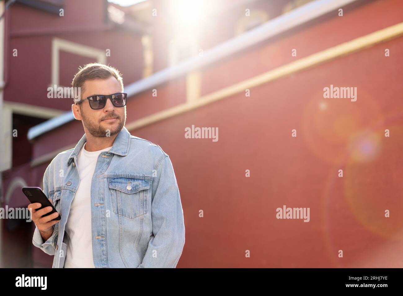 Bellissimo uomo che indossa una giacca in denim e occhiali da sole che cammina per la città. Foto Stock