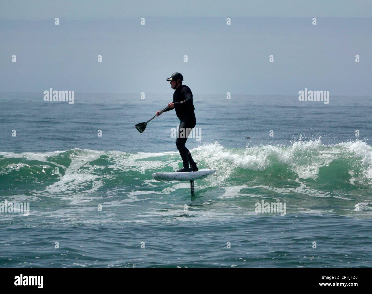 Un uomo con una muta cavalca un'onda su una tavola da surf in aliscafo, chiamata anche aliscafo, sulla costa pacifica dell'Oregon. Foto Stock