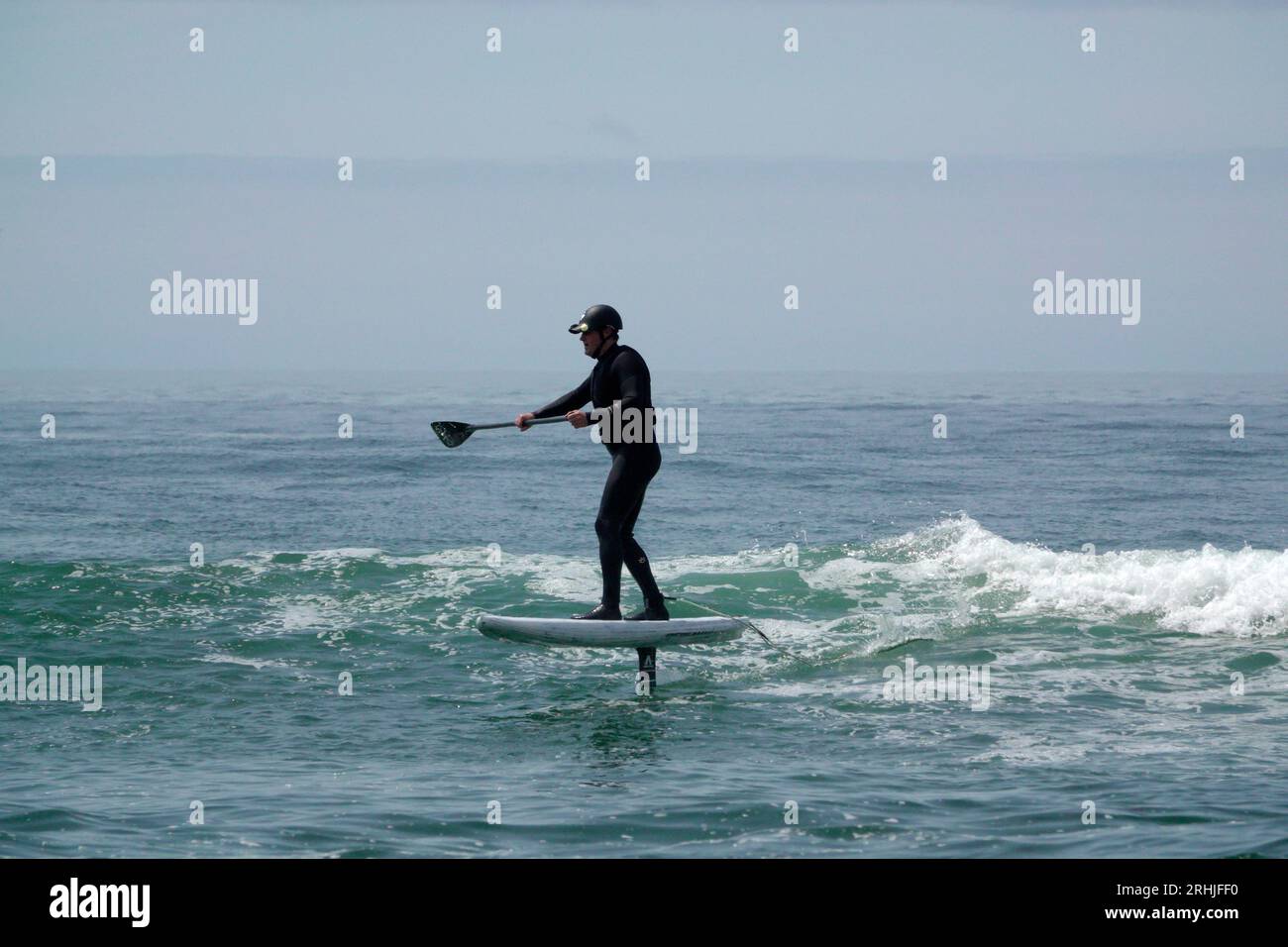 Un uomo con una muta cavalca un'onda su una tavola da surf in aliscafo, chiamata anche aliscafo, sulla costa pacifica dell'Oregon. Foto Stock