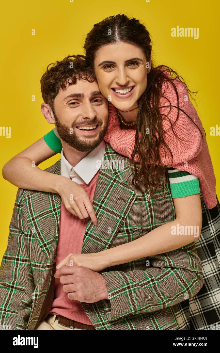 donna allegra che abbraccia un uomo barbuto, in blazer, sfondo giallo, abiti universitari, studenti felici Foto Stock