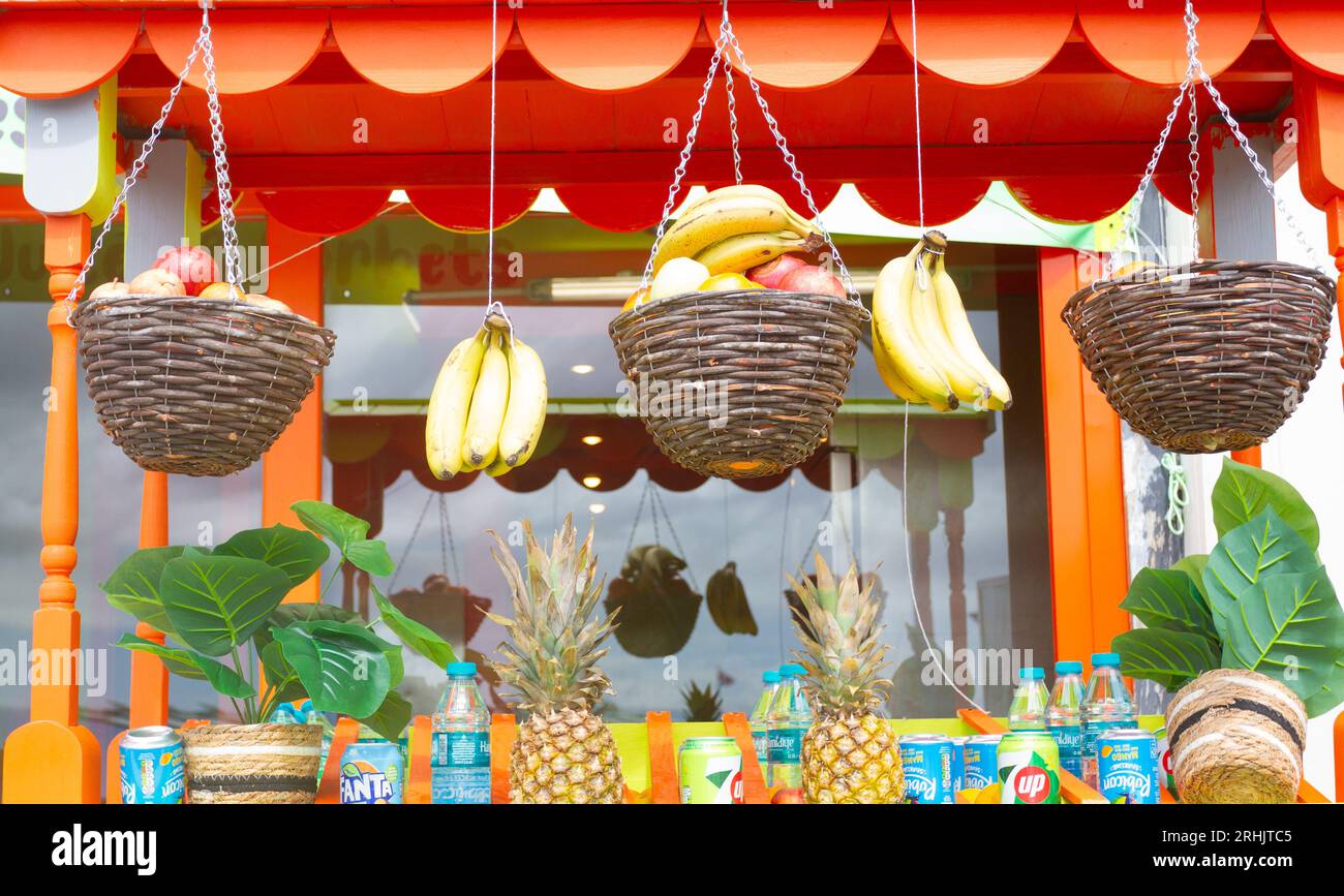 Primo piano di ciotole colorate di frutta, tra cui mele, banane e mele complete, oltre a bevande in vendita sul fronte di un negozio estivo lungo la costa. Foto Stock