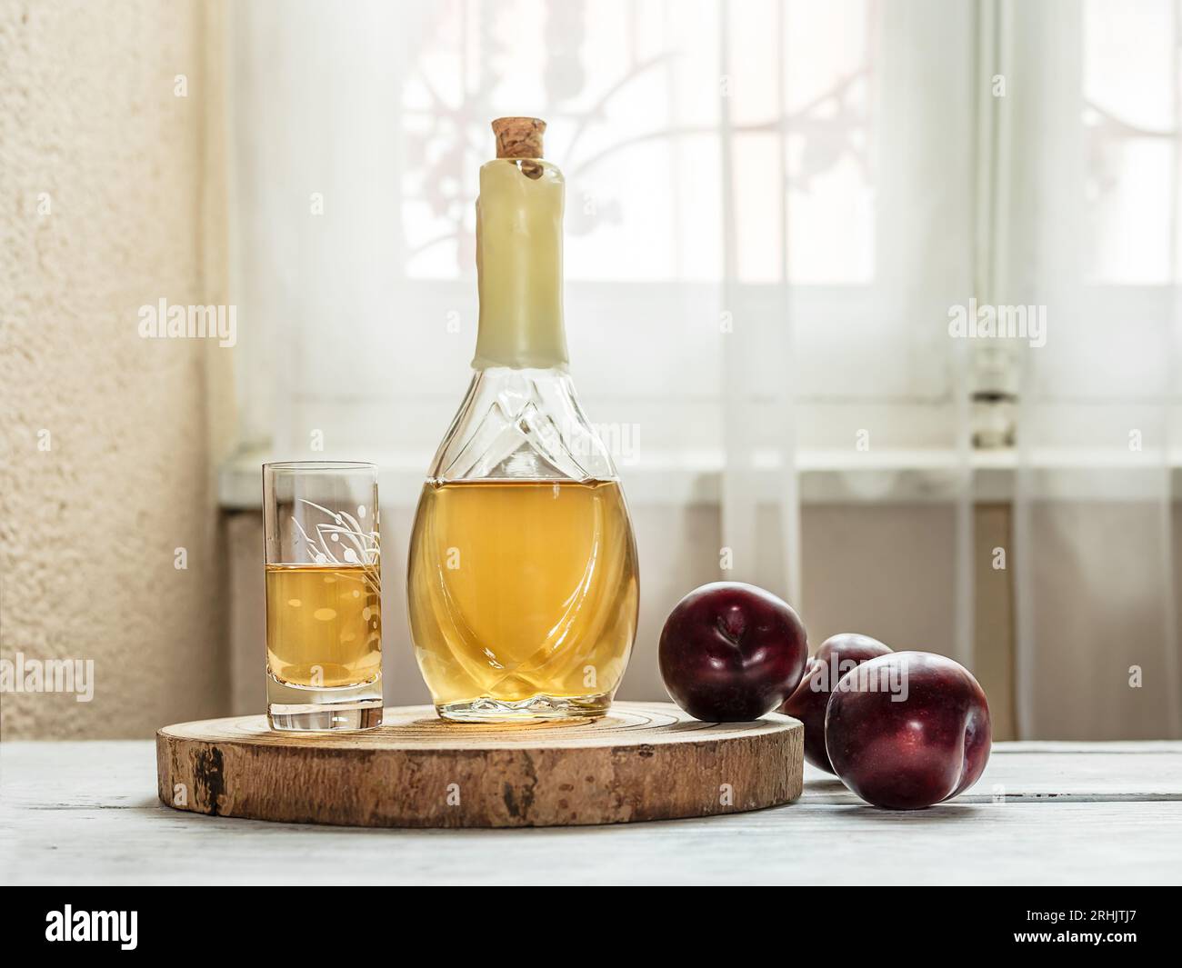 Brandy di prugne balcaniche - rakija o rakia slivovica in bottiglia, una wineglass con sljivovica e prugne fresche su sfondo chiaro vicino alla finestra. Foto Stock