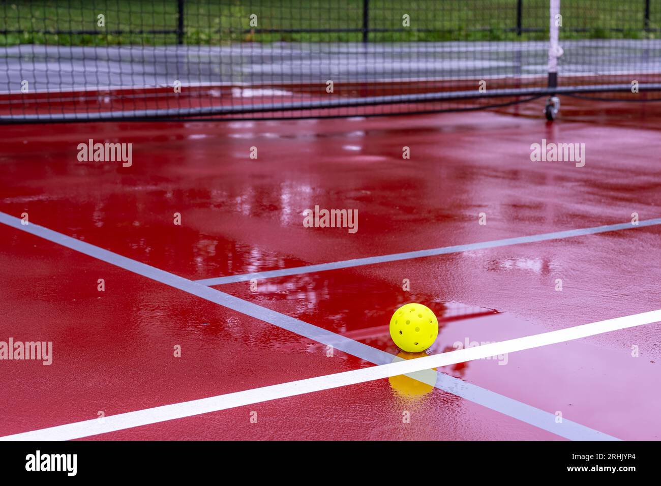 Una palla in piccino su un campo da tennis rosso bagnato con linee bianche combinate con linee grigie di picchiettia Foto Stock