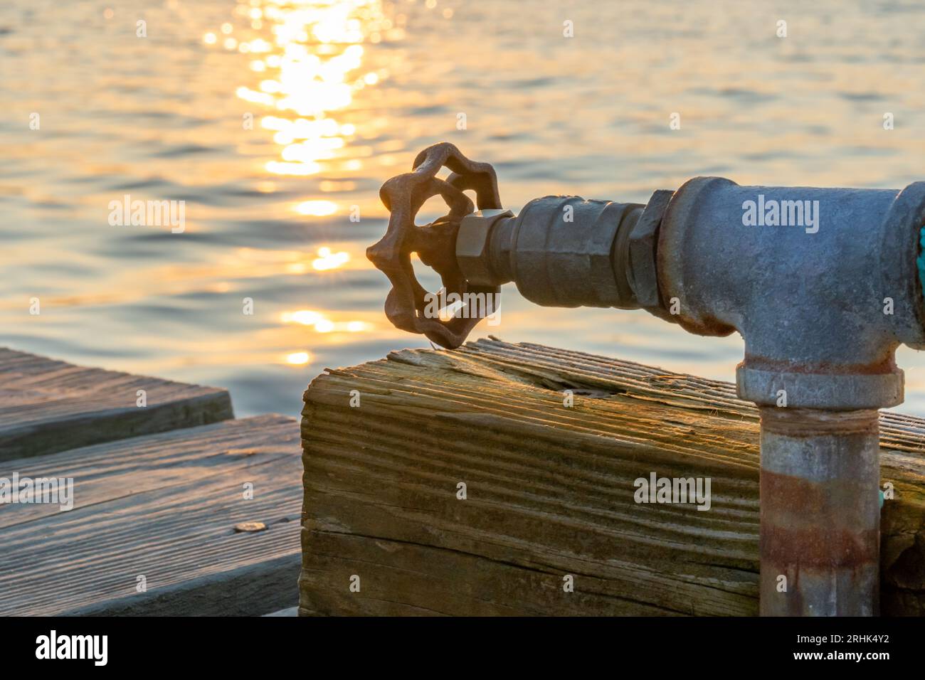 Rubinetto dell'acqua esterna, bavaglino, su un palo di legno presso un molo durante il tramonto. Foto Stock