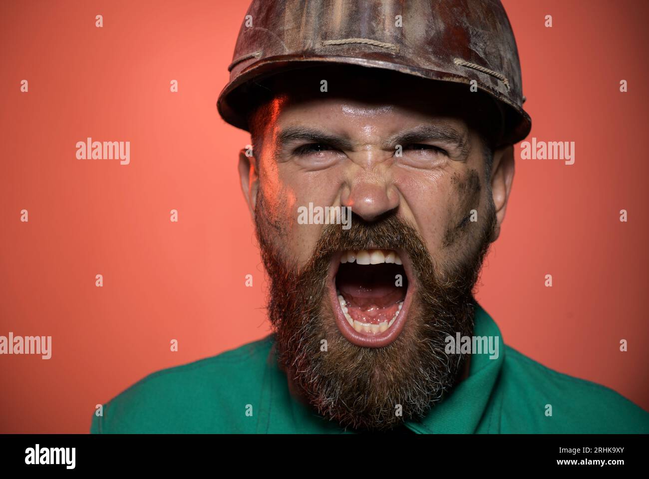 Ritratto di primo piano che urla l'operaio edile con elmetto. Costruttore arrabbiato nel casco di sicurezza. Grida uomo barbuto in uniforme da costruttore e hardhat Foto Stock