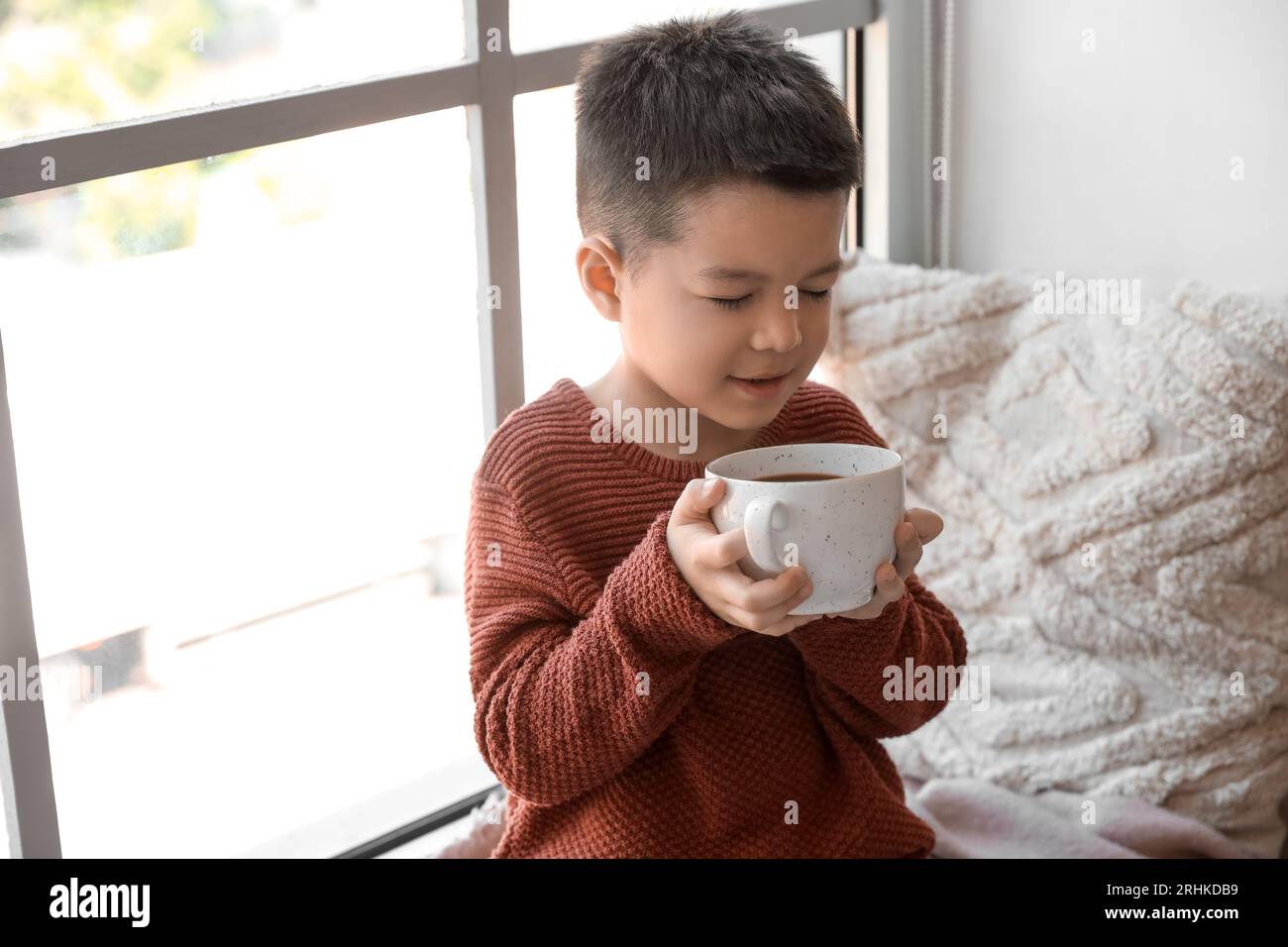 Simpatico bambino in maglia con una tazza di cacao a casa Foto Stock