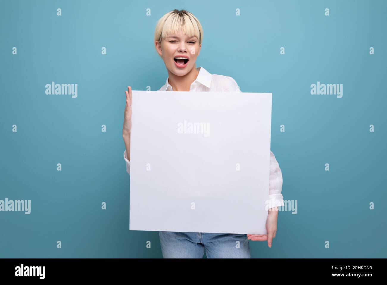 giovane lavoratrice bionda di successo in ufficio con una camicia bianca e un jeans tiene un pezzo di carta per inserire una pubblicità. concetto aziendale Foto Stock