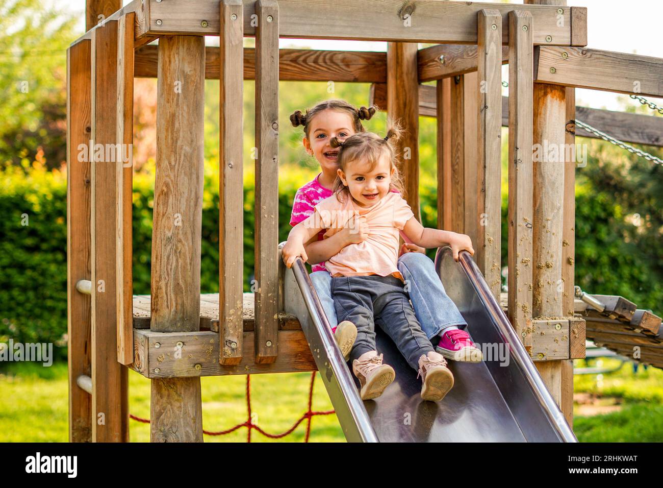Le sorelle scivolano insieme in un parco giochi - i bambini si divertono insieme Foto Stock