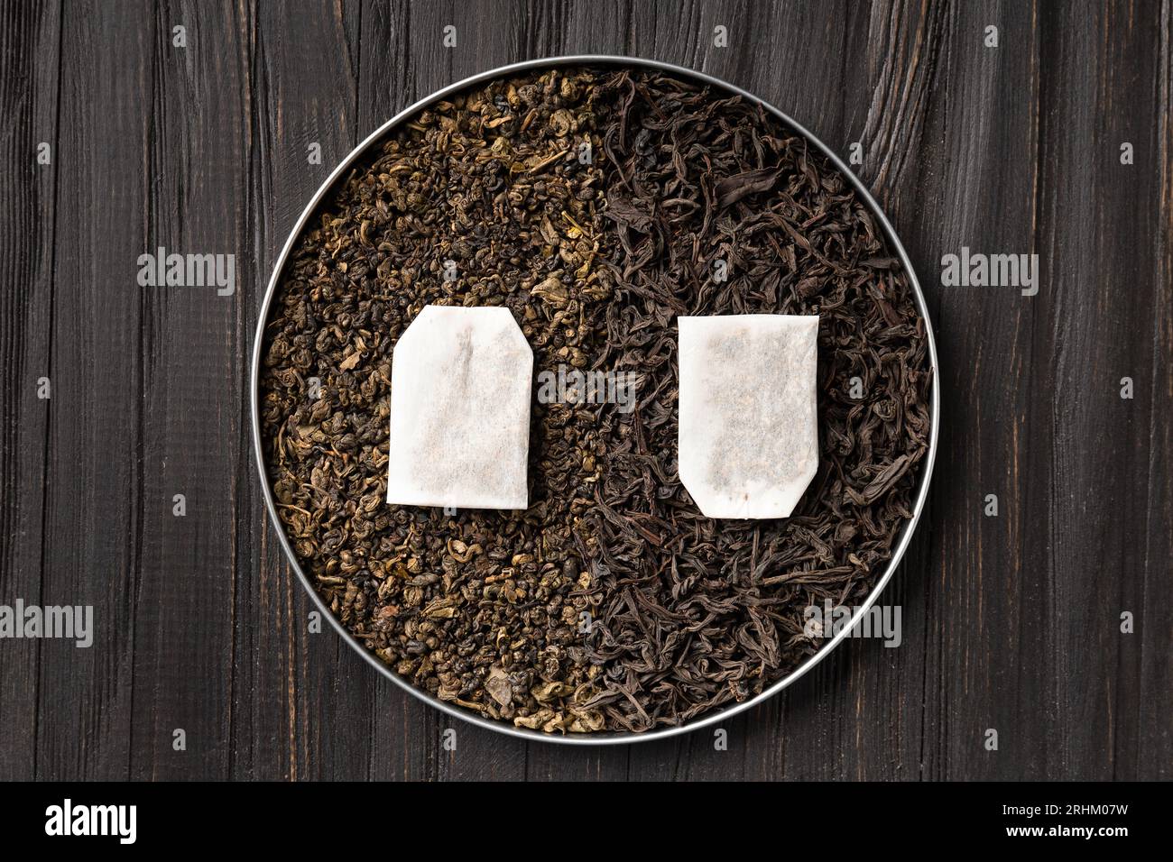 Composizione di foglie asciutte di tè verde, nero e bustine di tè su sfondo scuro, spazio per copia con vista dall'alto. Diversi tipi di tè su uno sfondo di legno Foto Stock