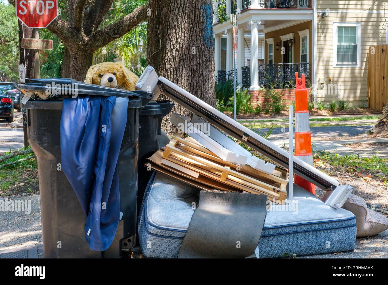 NEW ORLEANS, LOUISIANA, USA - 16 AGOSTO 2023: Giocattolo per animali imbottito, materasso e altri oggetti gettati all'interno e intorno ai cestini della spazzatura sul marciapiede Foto Stock