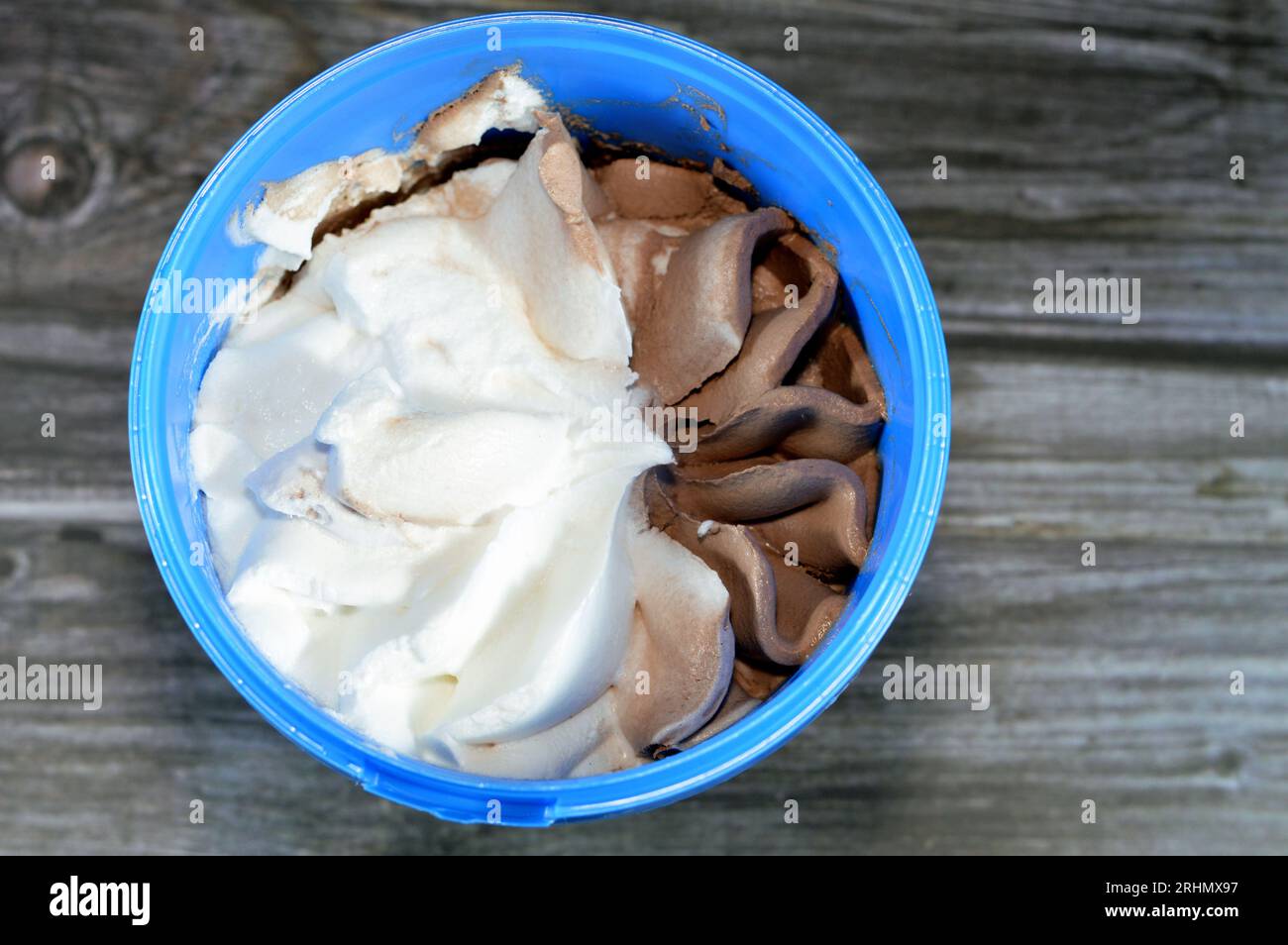 Gelato congelato bianco alla vaniglia e cioccolato in una ciotola di plastica isolata su fondo di legno e pronta per essere servita, gelato al cioccolato alla vaniglia Foto Stock