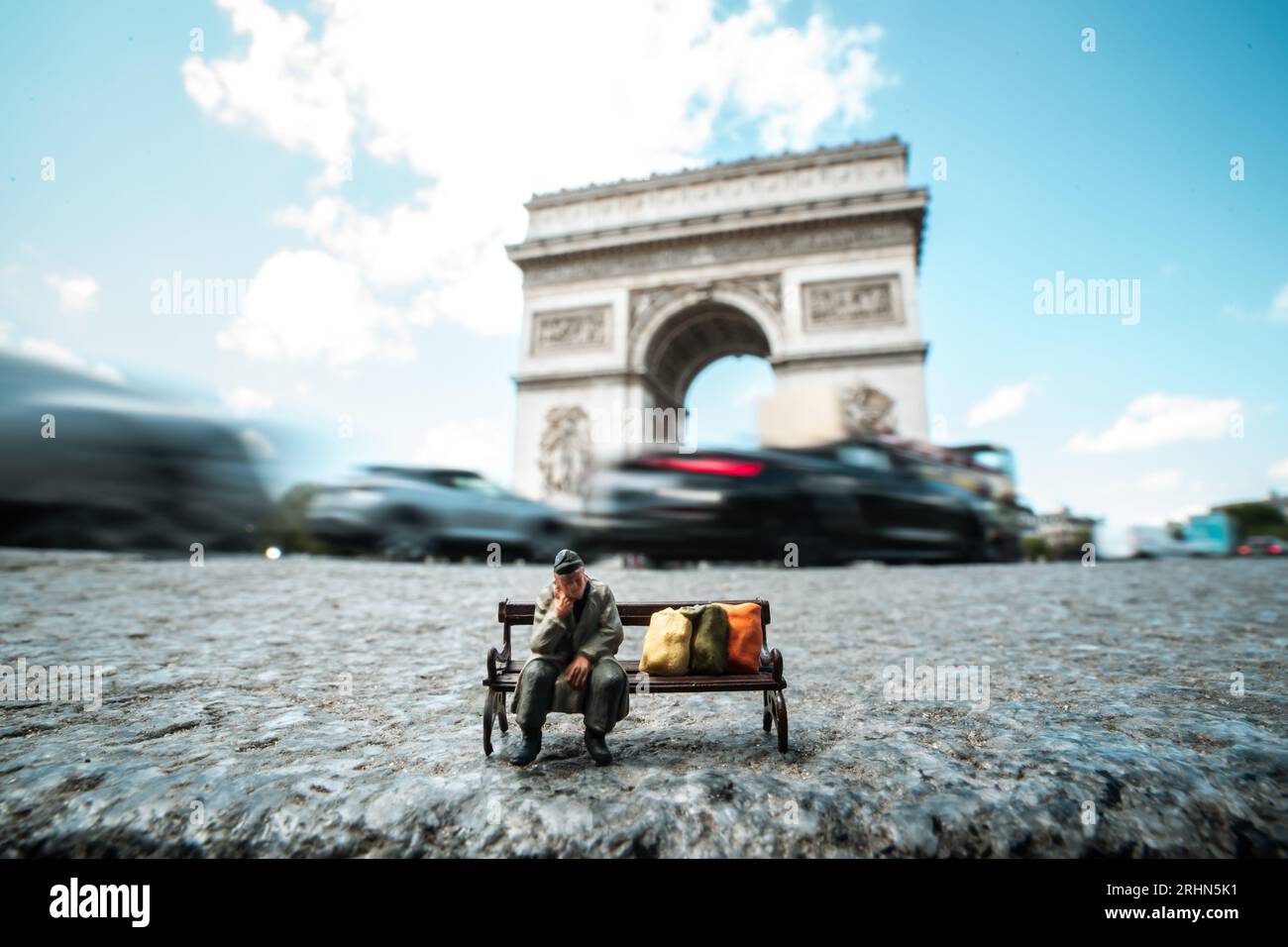 Un senzatetto in miniatura siede su una panchina di fronte all'Arco di Trionfo, Parigi, Francia Foto Stock