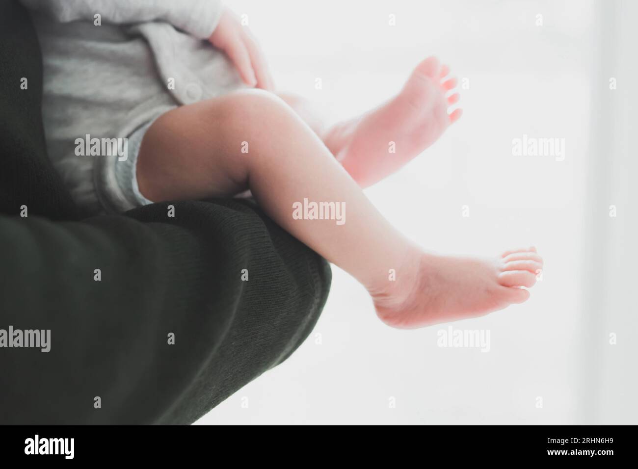 Genitore che tiene il bambino, primo piano delle gambe e dei piedi del bambino Foto Stock