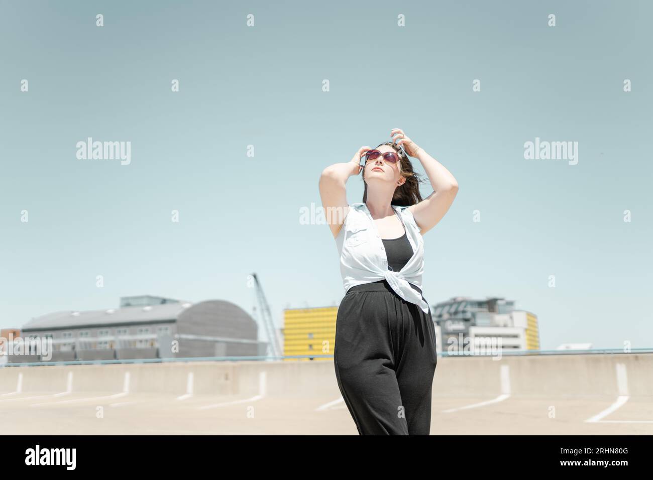 Una donna che si fissa i capelli e guarda il cielo in un paesaggio urbano Foto Stock