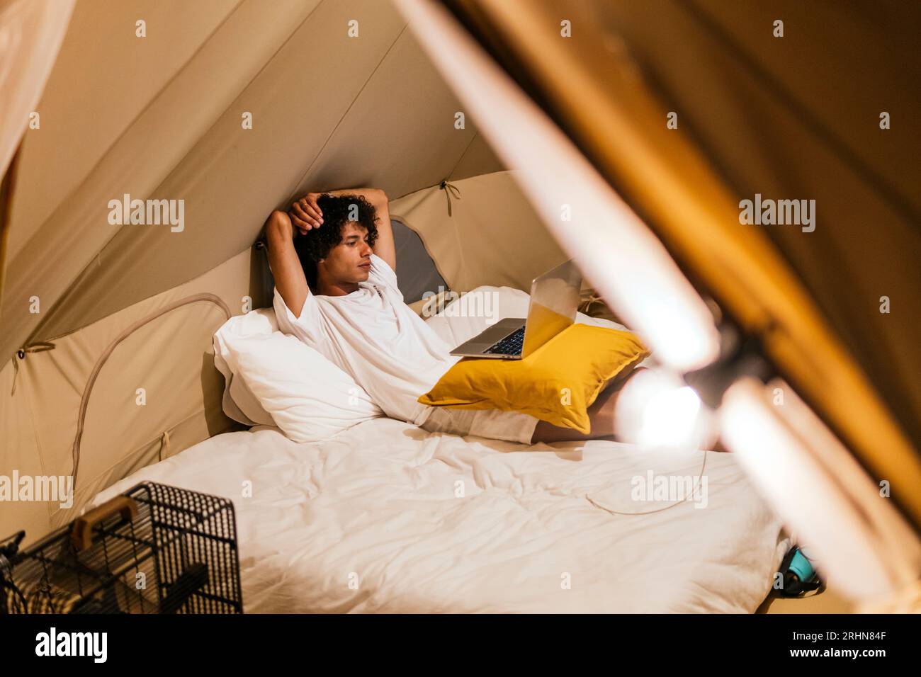 uomo latino che guarda una serie al computer sdraiato sul letto in una tenda Foto Stock