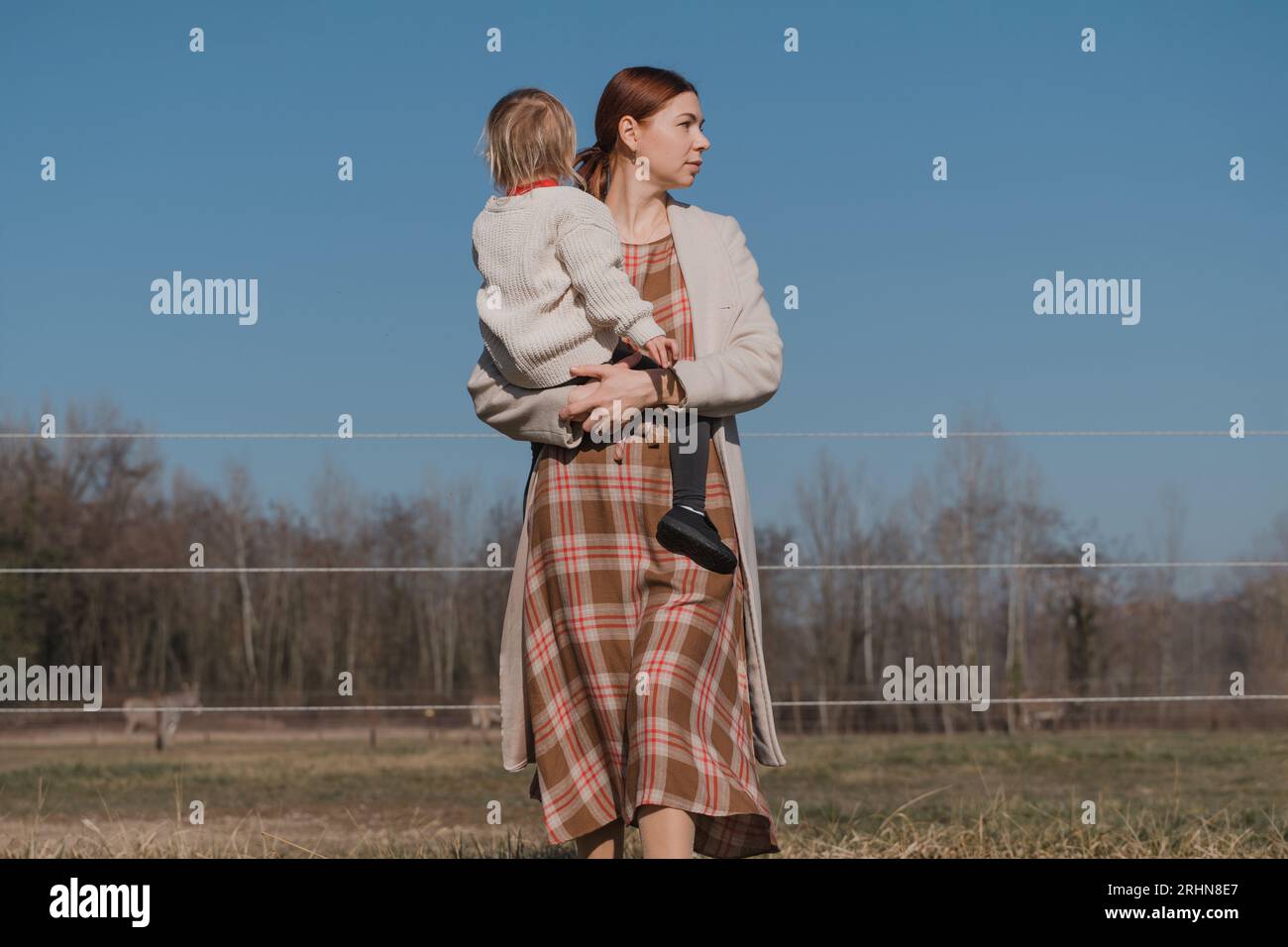 La donna con un bambino tra le braccia cammina nel campo, sembra seria Foto Stock