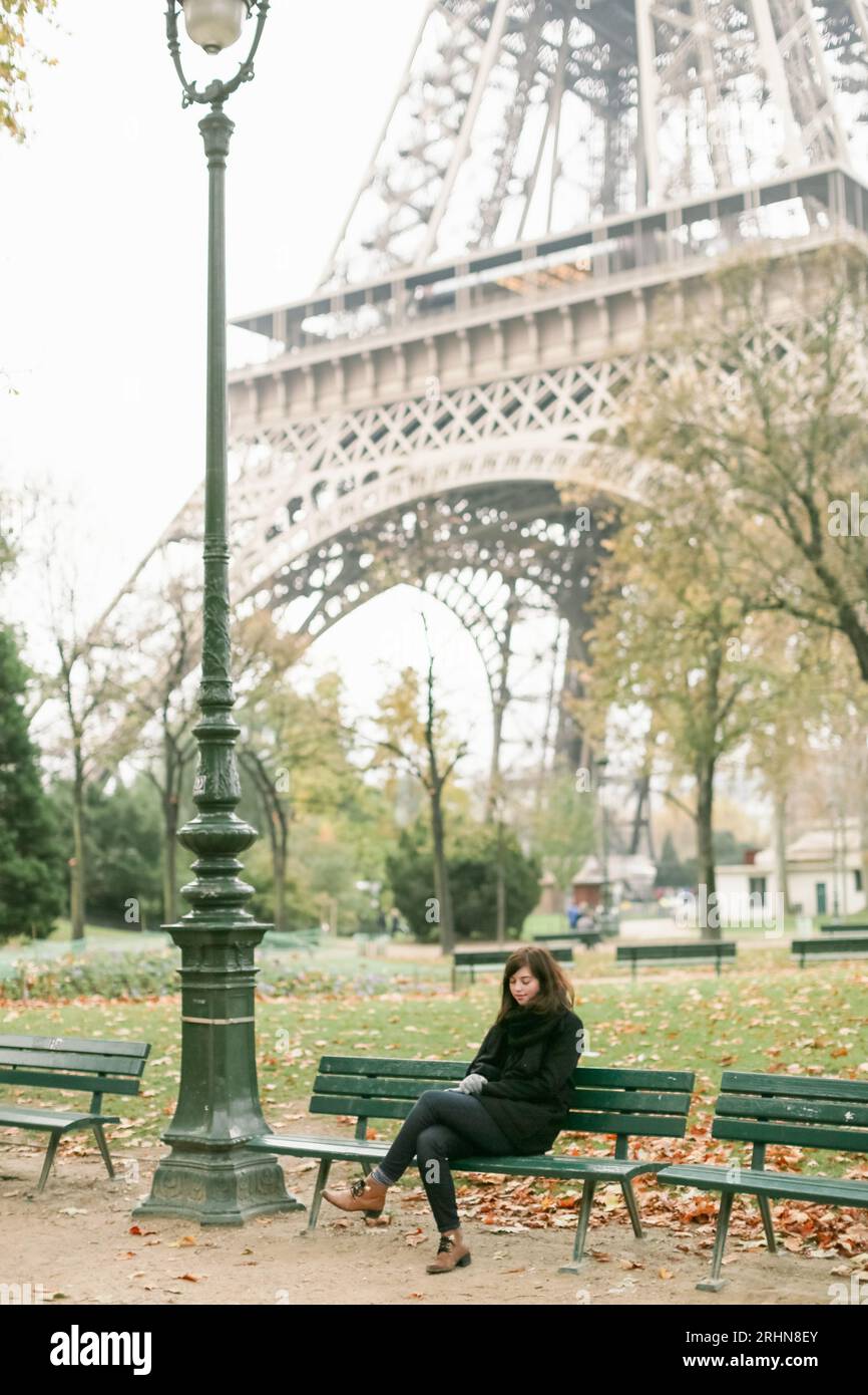 Donna a Parigi seduta su una panchina che si affaccia sulla Torre Eiffel Foto Stock