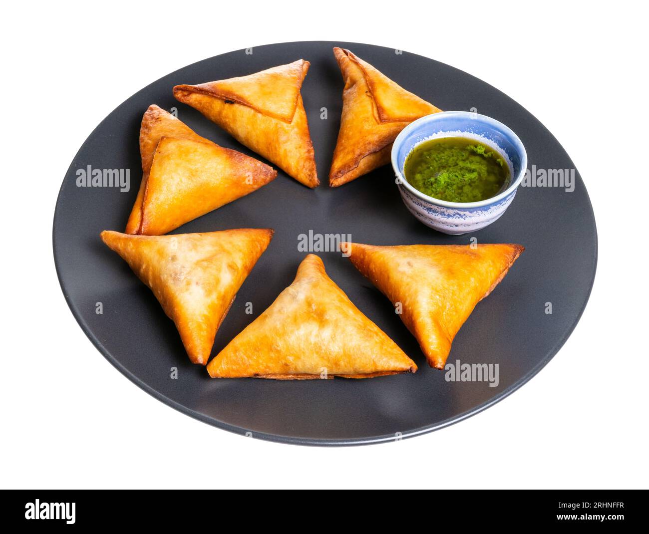 porzione di empanadas fritte triangolari su piatto rotondo nero con ritaglio di salsa su sfondo bianco Foto Stock