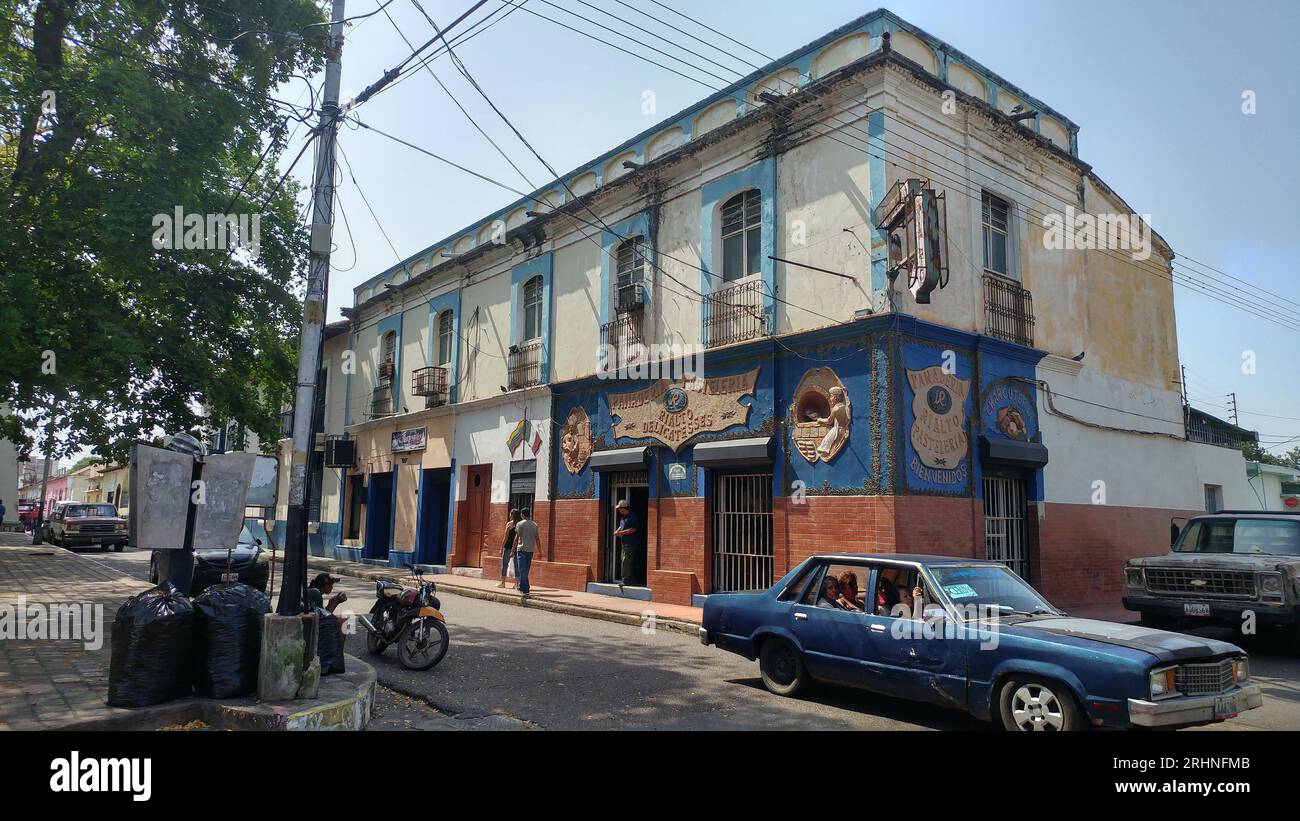 Foto che mostra la vita pubblica in una strada della città di Calabozo in Venezuela, raffigurata che mostra alcuni vecchi edifici, vecchie auto e persone. Foto Stock