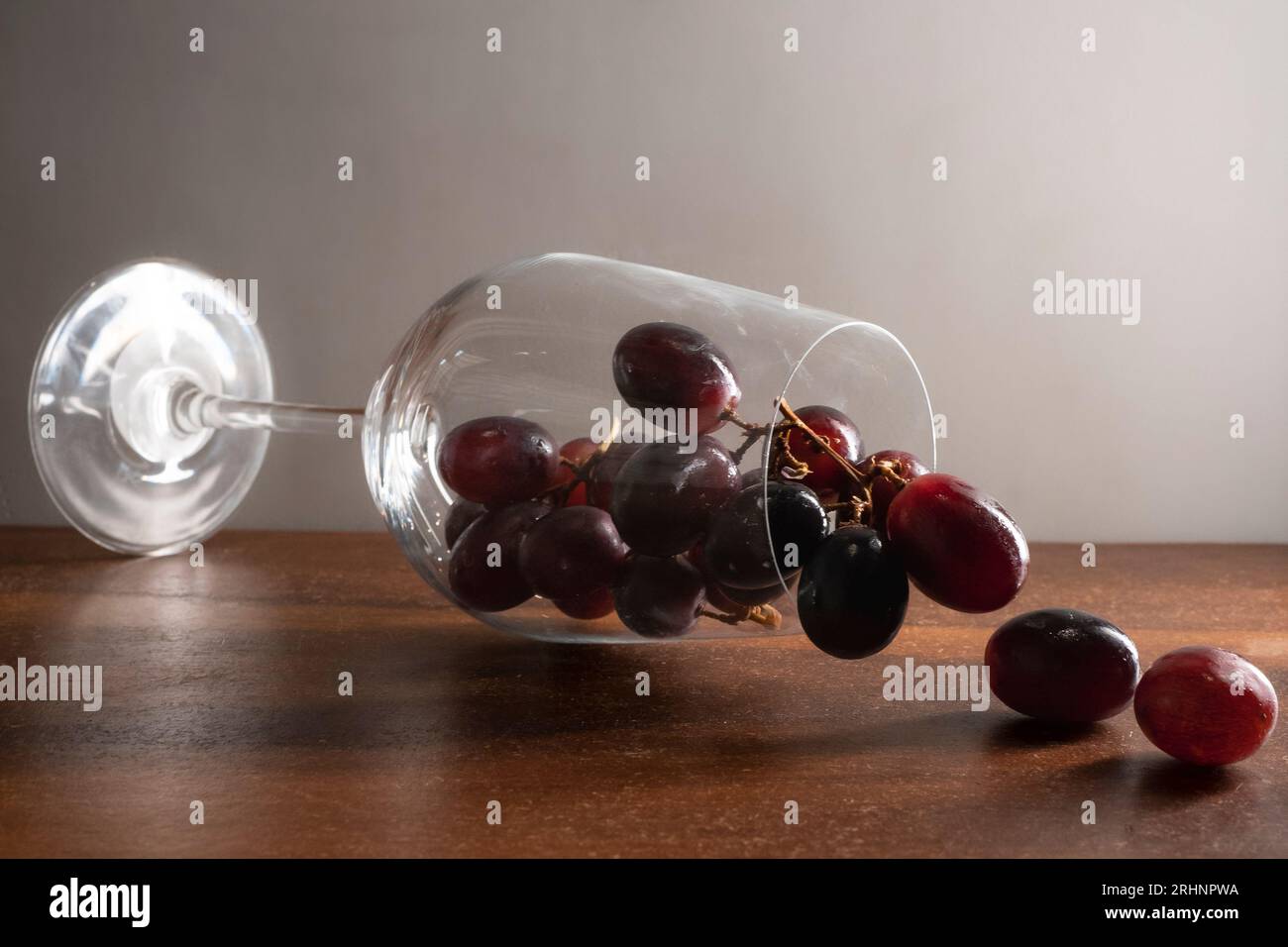 Un bicchiere di vino che cade su un tavolo di legno e uva rossa scura che scorre su sfondo bianco Foto Stock