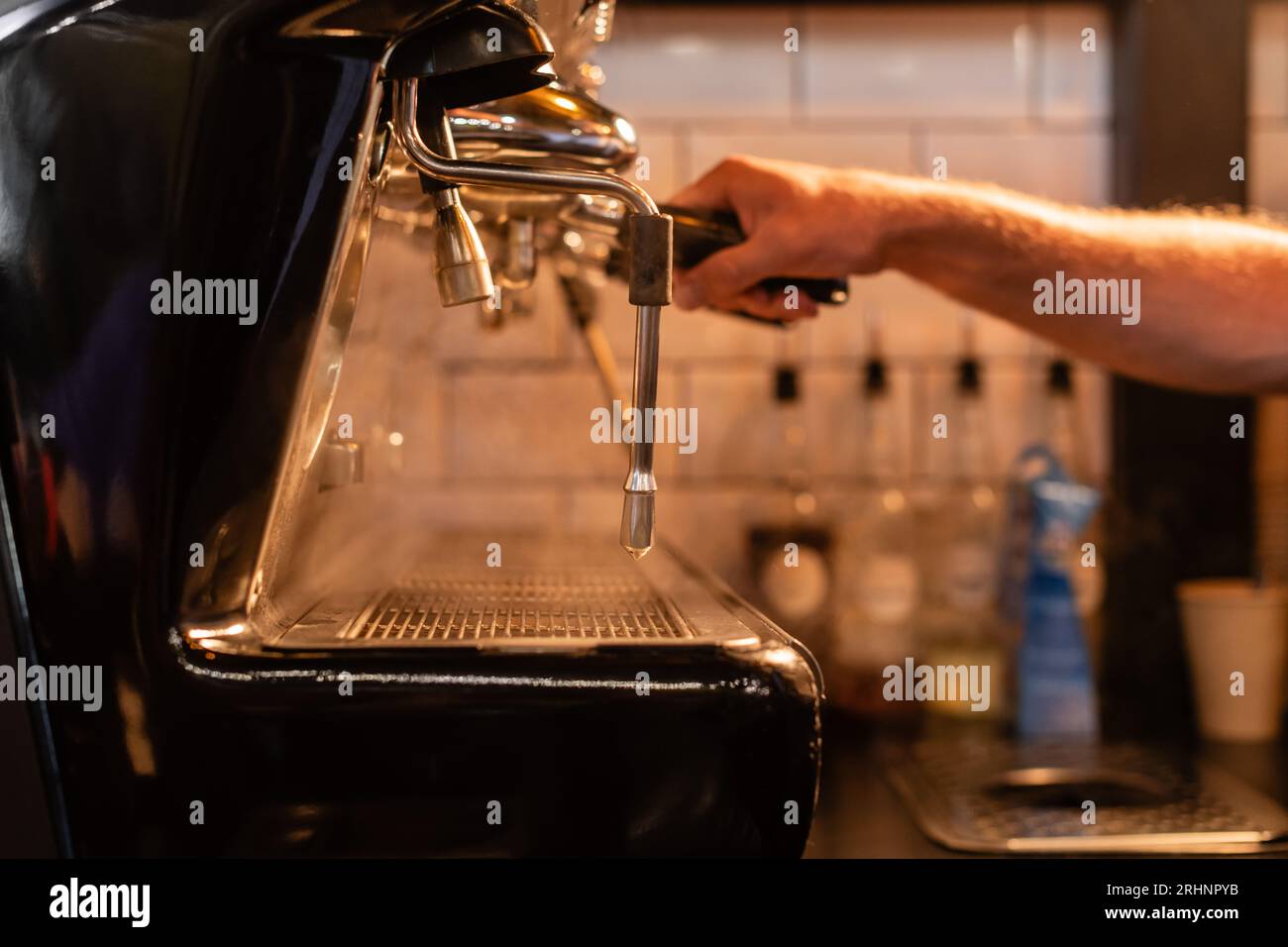 vista ritagliata del barista sfocato utilizzando la macchina da caffè vicino al vapore e all'illuminazione della caffetteria Foto Stock