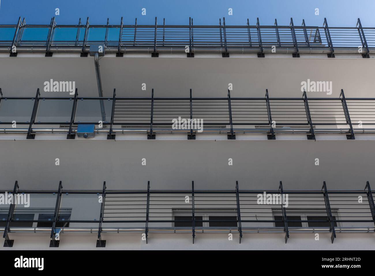 Vista dal basso verso l'alto dalla facciata di un edificio moderno con balsoni e corrimano in acciaio e con un cielo azzurro Foto Stock