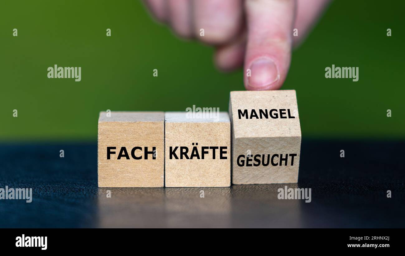 A mano gira il cubo di legno e cambia l'espressione tedesca "Fachkraefte gesucht" (lavoratori qualificati ricercati) in "Fachkraeftemangel" (richiesta di lavoratori qualificati) Foto Stock