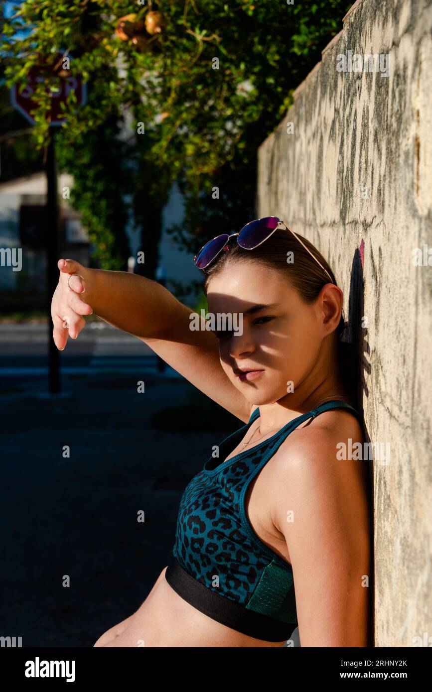 Bella donna che tiene la mano sopra gli occhi, schermando il viso dai raggi del sole. Appoggiandosi contro il muro, concetto di protezione, cancro della pelle, macchina della pelle Foto Stock