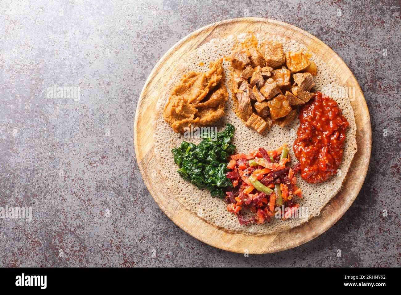Injera etiope condita con carne, verdure, verdure e verdure da vicino sulla tavola di legno sul tavolo. Vista superiore orizzontale dall'alto Foto Stock