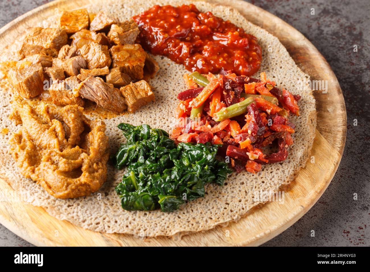 Injera etiope condita con carne, verdure, verdure e verdure da vicino sulla tavola di legno sul tavolo. Orizzontale Foto Stock