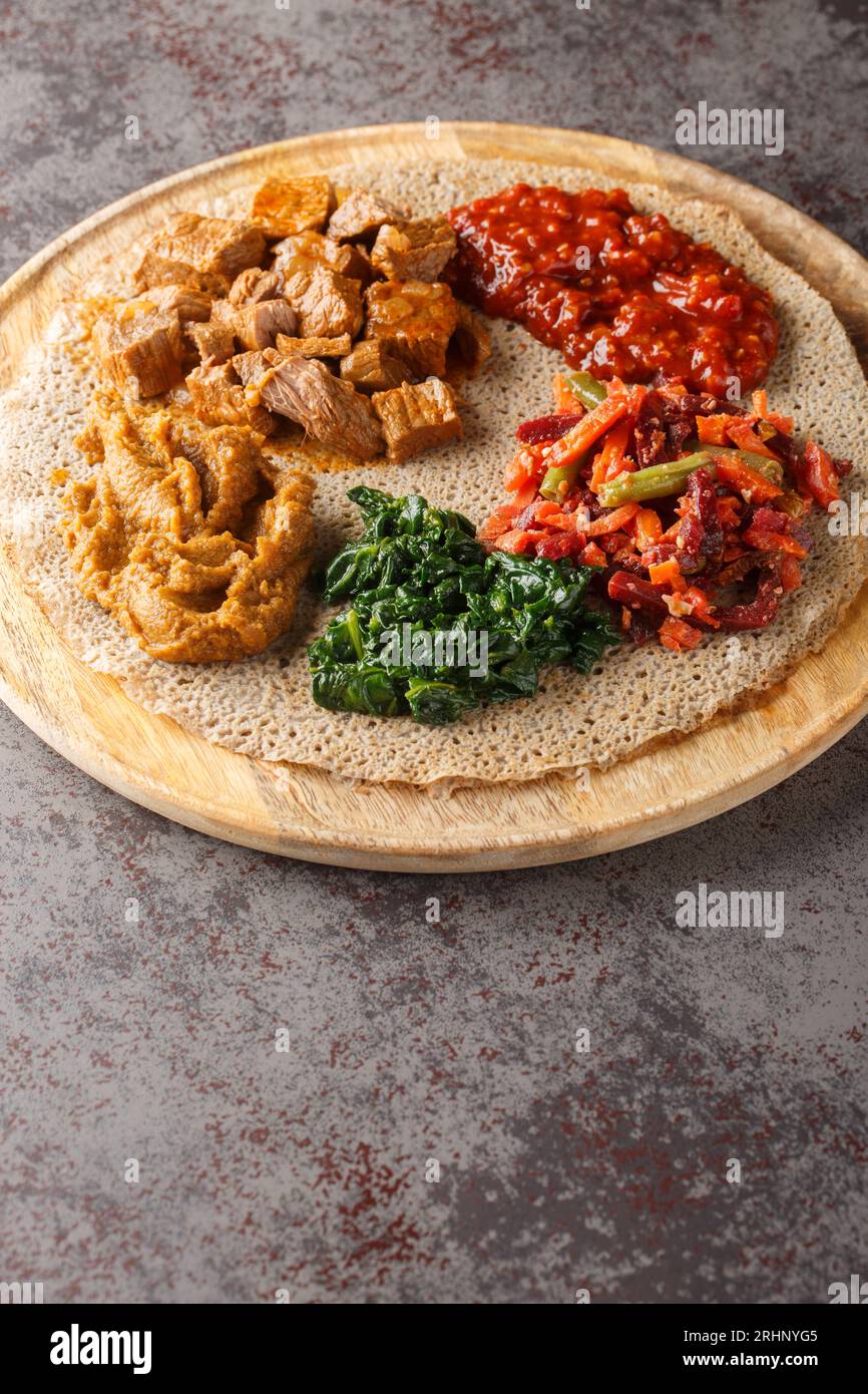 I pasti consistenti in injera e diversi tipi di stufato wat o tsebhi sono tipici della cucina etiope primo piano sulla tavola di legno. Verticale Foto Stock