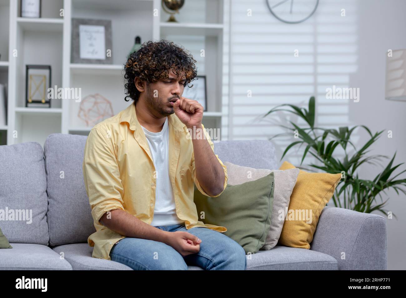 Uomo freddo malato seduto da solo sul divano a casa, ispanico ha bronchite tossisce respiro corto. Foto Stock