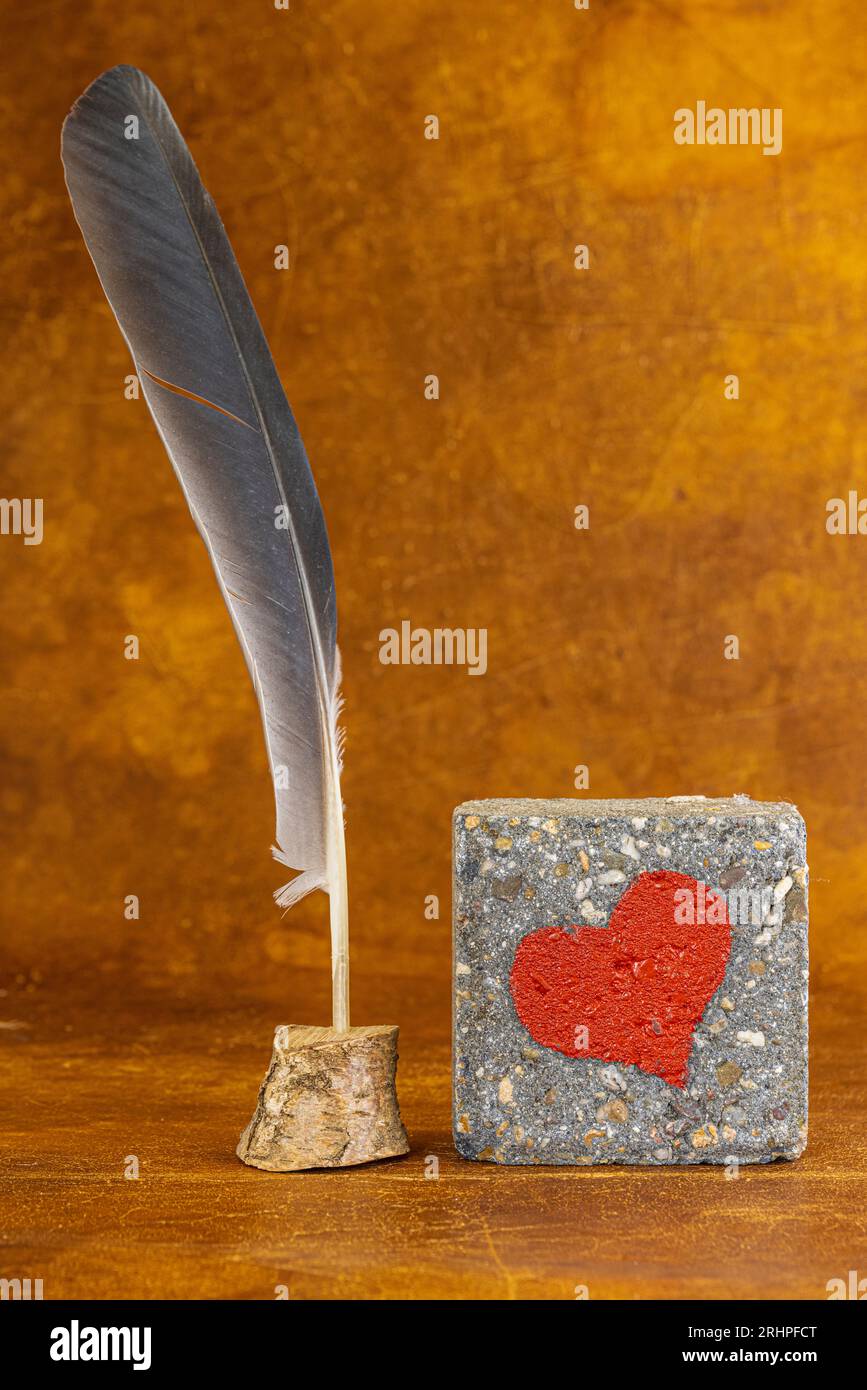 Una piuma e pietra con cuore rosso, immagine simbolo, decorazione, natura morta Foto Stock