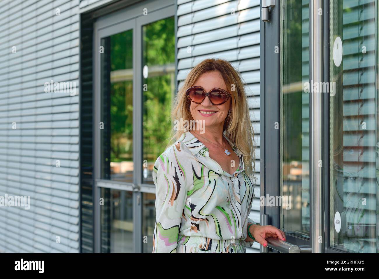 La donna con gli occhiali da sole entra in un moderno edificio industriale e sorride alla macchina fotografica Foto Stock