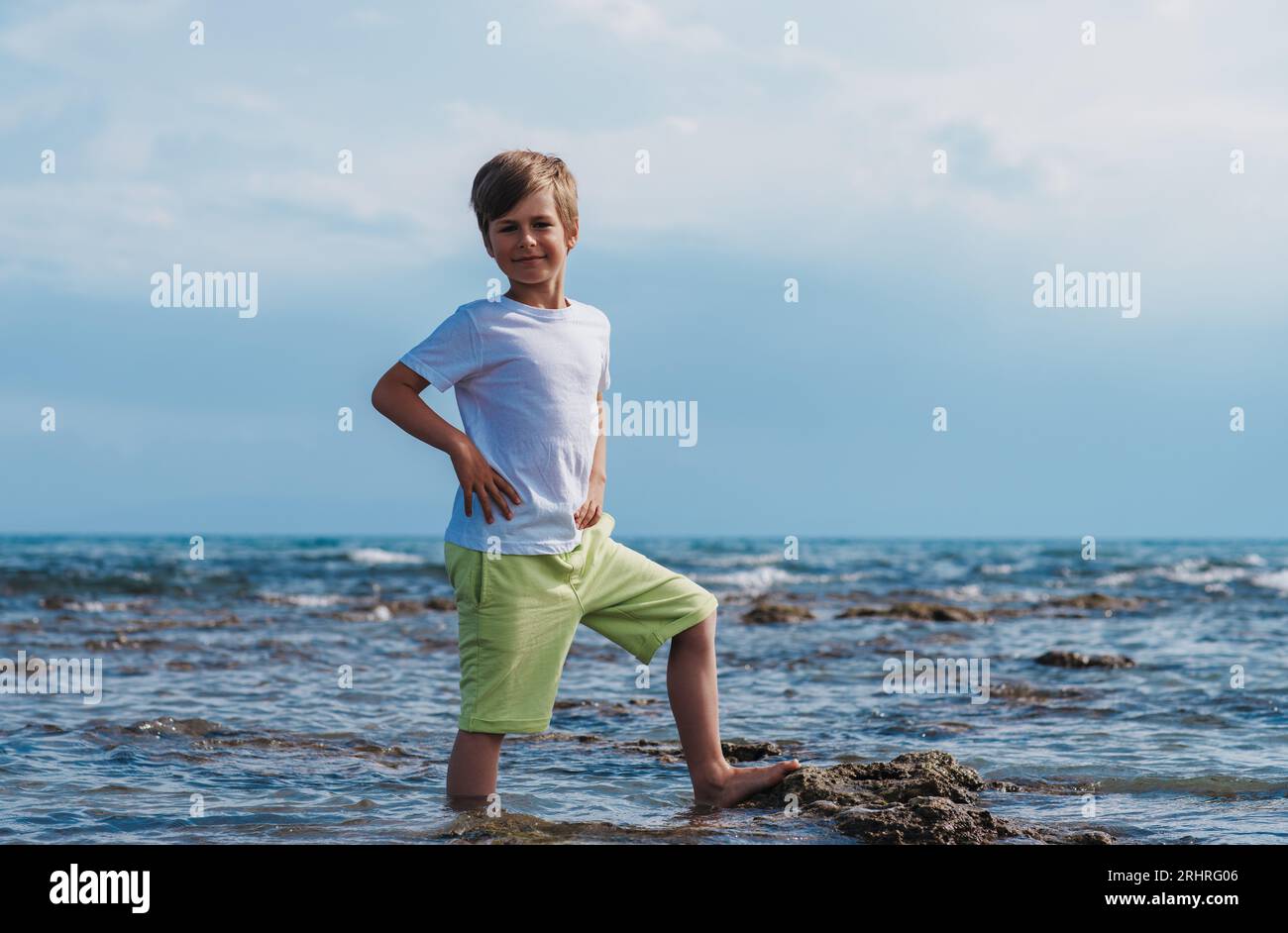 Ritratto di un felice bambino di sette anni in piedi in acqua vicino al mare in estate Foto Stock