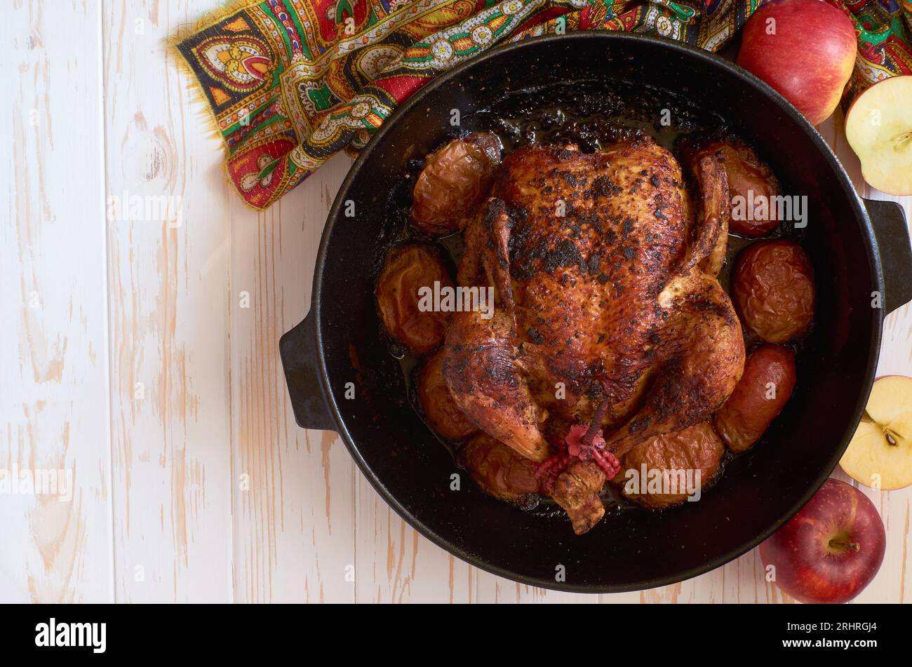 Pollo arrosto al forno con mele in padella di ghisa decorato con tovagliolo colorato su sfondo di legno bianco da tavola, fla Foto Stock