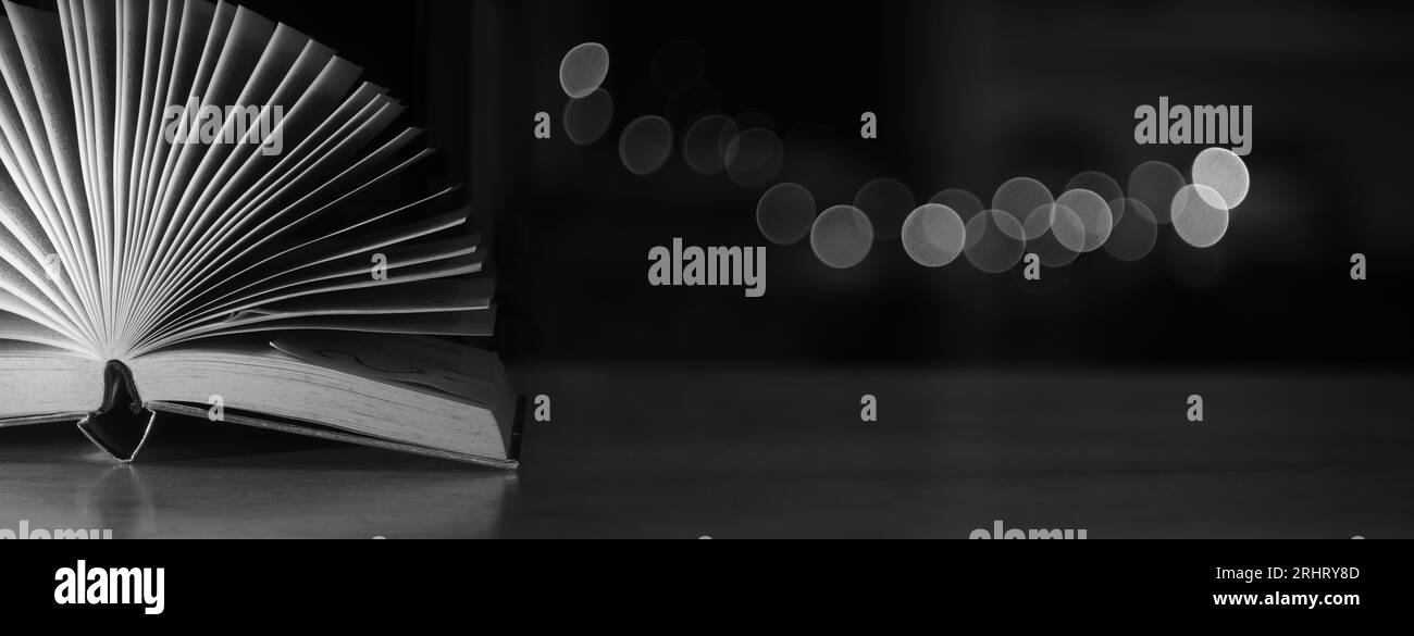 Libro aperto, libro sul retro su tavolo di legno su sfondo scuro sfocato di palline bokeh. Ritorno a scuola, istruzione, lettura. Ampio spazio di copia Foto Stock