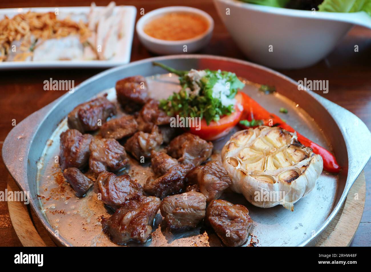 Deliziosa bistecca di manzo a dadini su un piatto caldo sfrigolante con contorni sfocati sullo sfondo Foto Stock
