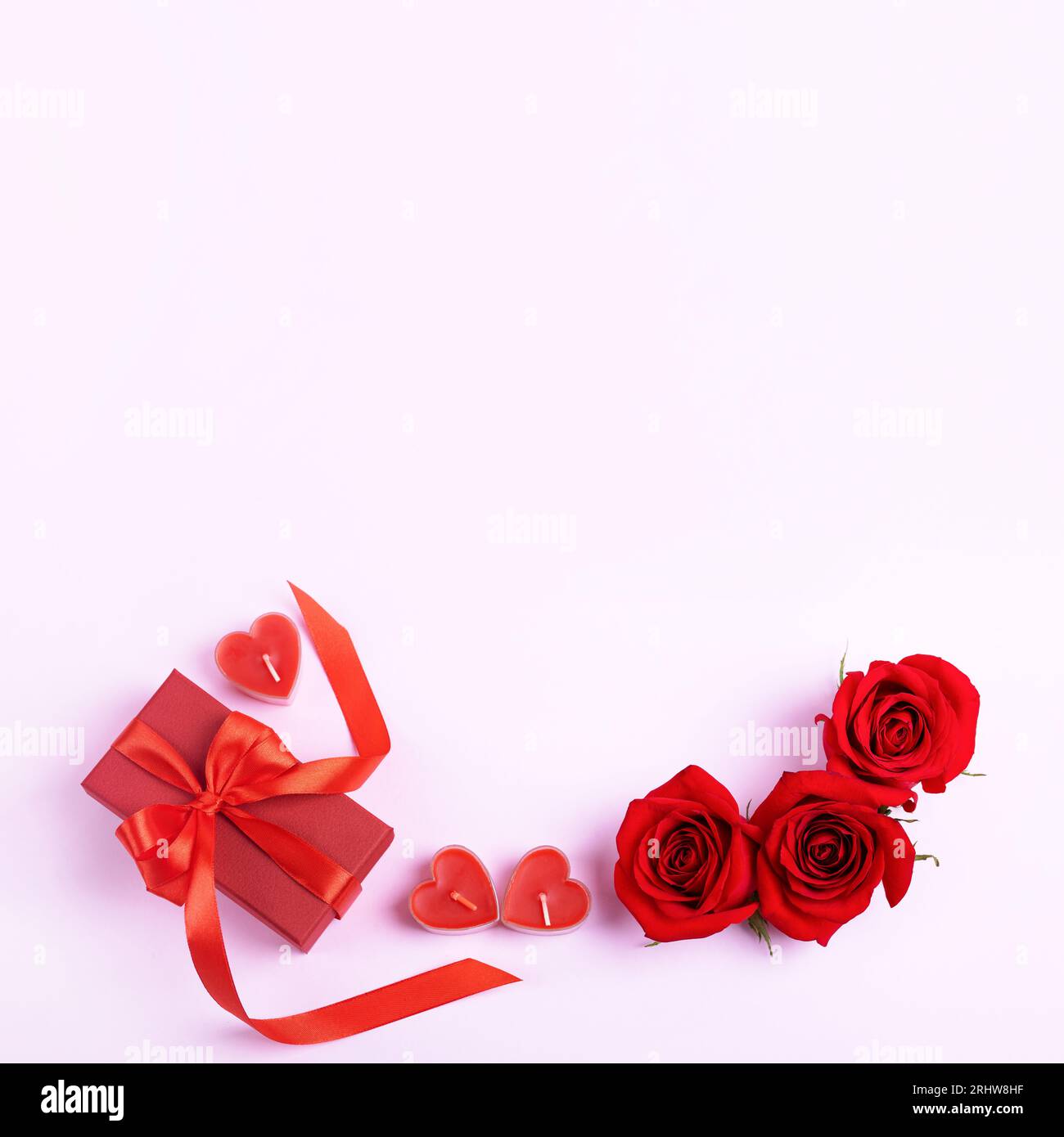 Rose rosse e confezione regalo rossa con fiocco di raso rosso e candele a forma di cuore. Sfondo romantico con spazio per il testo. Buon saluto auto Foto Stock