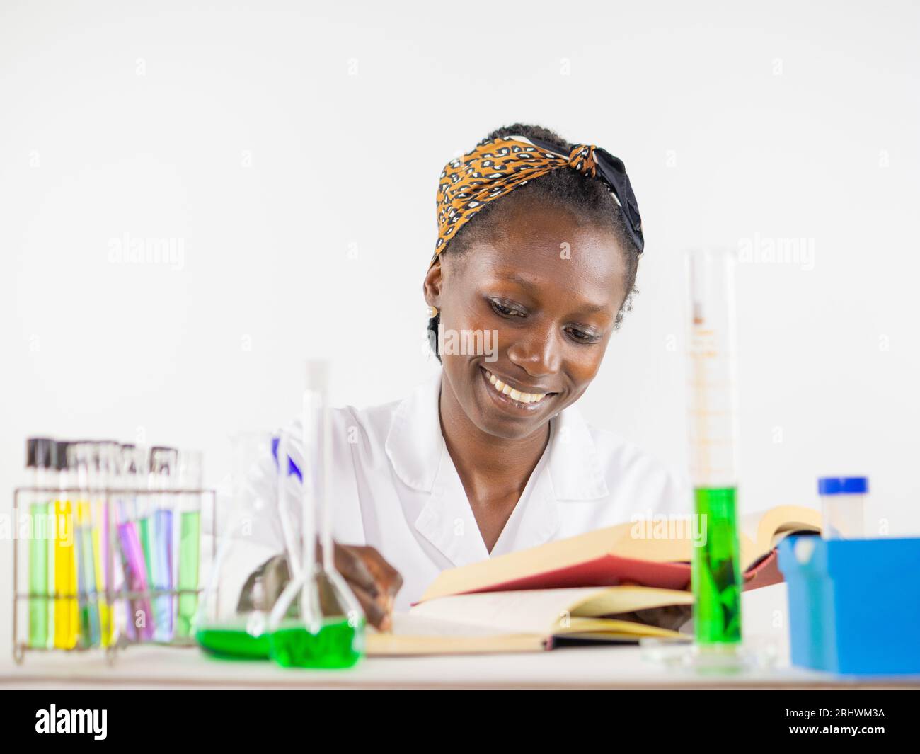 Giovane scienziata che fa le sue ricerche in laboratorio mentre consulta un libro di testo. Foto Stock