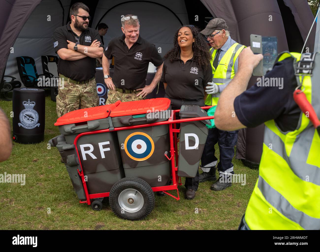 Eastbourne, Regno Unito. 19 agosto 2023. Un anziano bin municipale con i suoi bidoni dipinti nei colori del mimetismo militare e con una rosa della RAF posa per una foto con i membri del team della RAF Battle of Britain Memorial Flight nella mostra militare accanto all'annuale Eastbourne Airbourne, un airshow internazionale. Lo spettacolo si svolge per quattro giorni con esibizioni di volo lungo il lungomare. Crediti: Andy Soloman/Alamy Live News Foto Stock