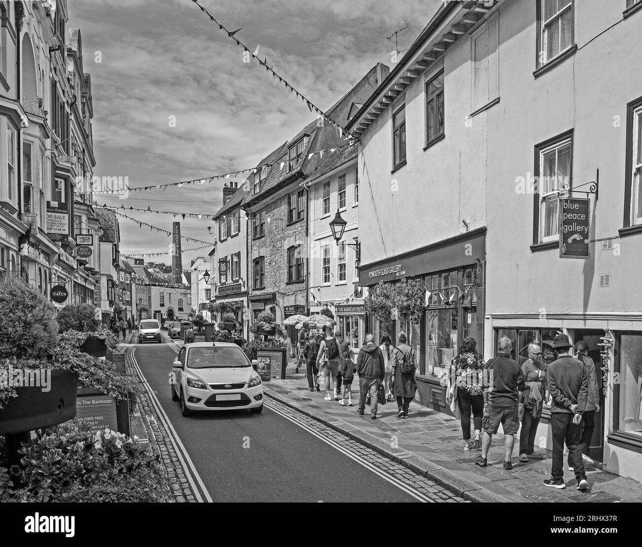 L'immagine monocromatica di vasche di fiori e bunting donano un'atmosfera celebrativa a Southside Street, nello storico Barbican di Plymouth. Un eccentrico mix di piccoli negozi, Foto Stock