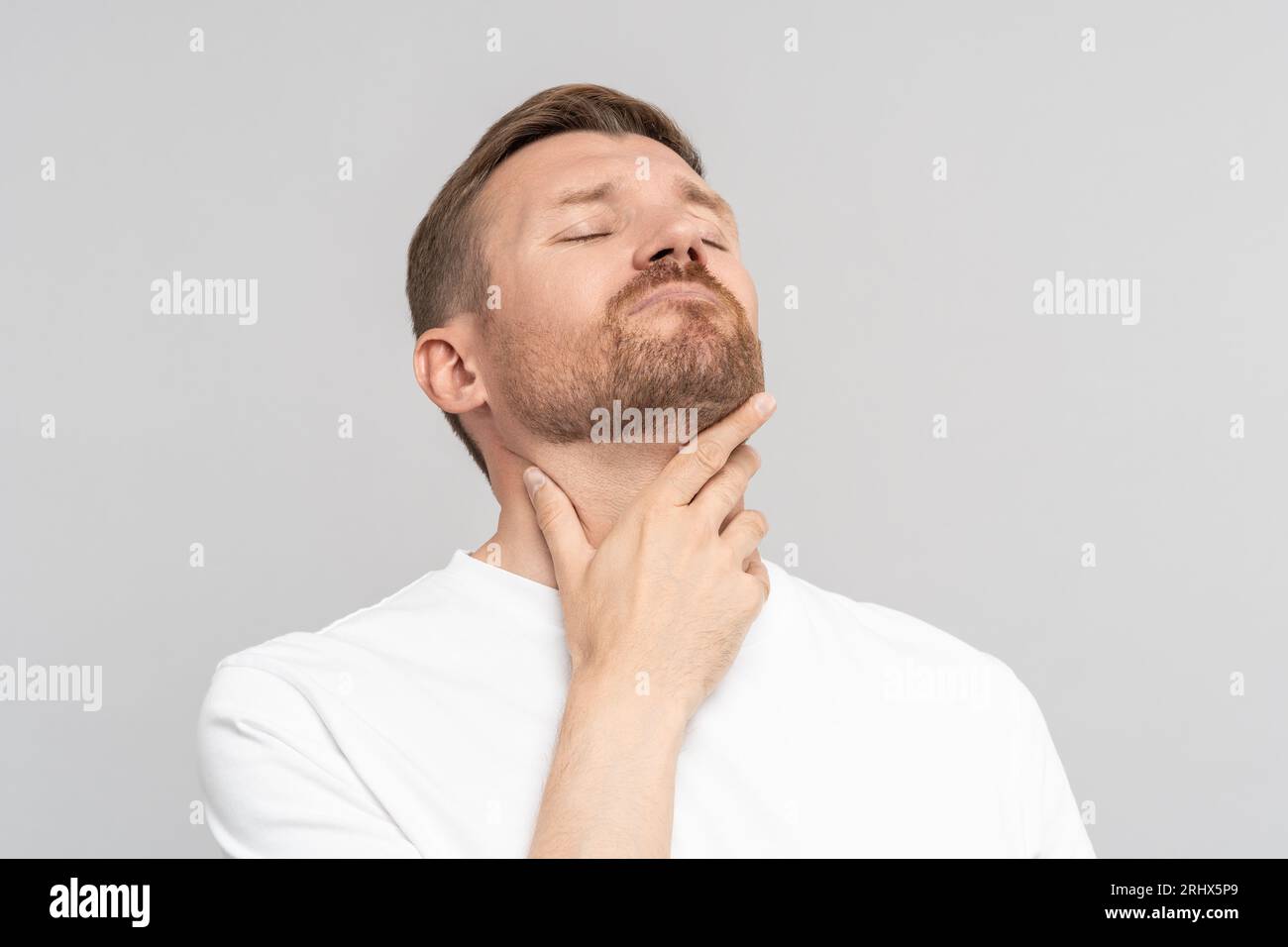 L'uomo tiene il collo, soffre di mal di gola. Freddo, malattia. Isolato su sfondo grigio Foto Stock