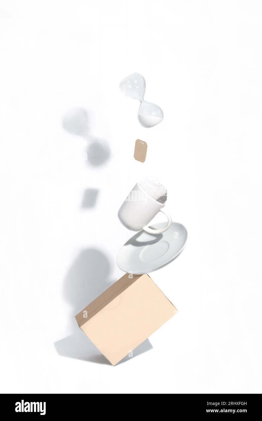 Composizione bilanciata con una scatola, un piatto, una tazza di tè bianco e una clessidra su sfondo bianco Foto Stock