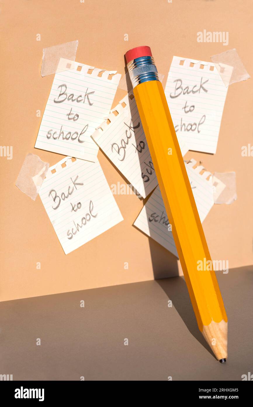 Matita di colore giallo con gomma rossa e punta rotta appoggiata su pareti beige con ombre vicino a carte incollate da quaderno a spirale con messag Foto Stock