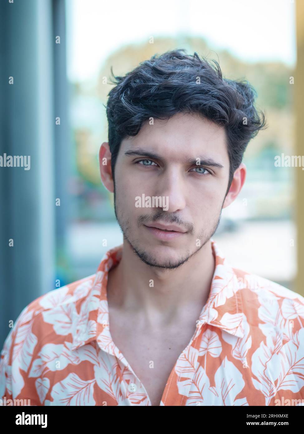 La testa e le spalle hanno girato di un bel giovane uomo con occhi verdi in ambiente urbano, guardando la macchina fotografica, indossando una t-shirt Foto Stock