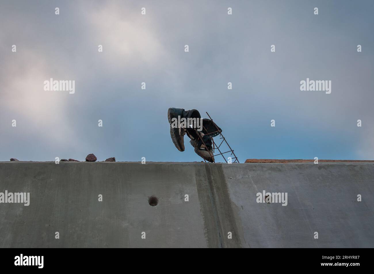 Stivali da lavoro neri legati a tondini dietro una parete di cemento in un cantiere edile. Foto Stock