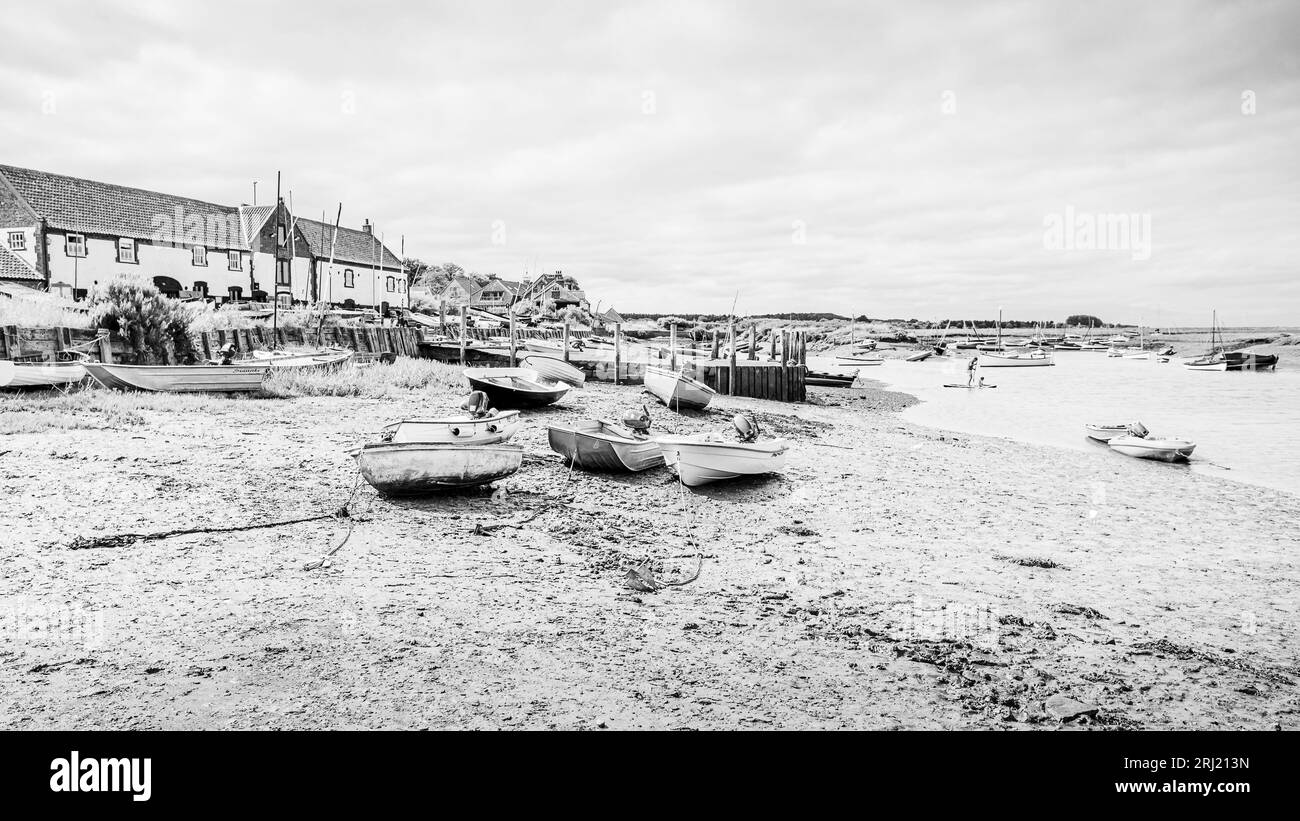 Le barche fiancheggiano il fangoso litorale di Burnham Overy Staithe raffigurato in bianco e nero sulla costa del Norfolk settentrionale nell'agosto 2023. Foto Stock