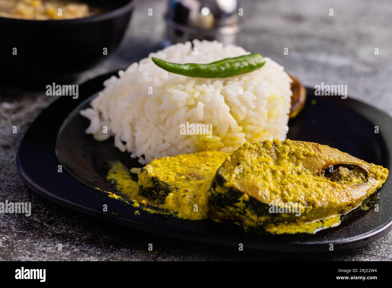 Curry di pesce Hilsa con pasta di senape e peperoncino verde servito su piatto insieme al riso a fuoco selettivo Foto Stock